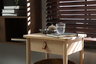 Photo of Wooden side table with glass of water, notebook and air reed diffuser indoors