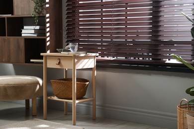 Photo of Wooden side table with glass of water, notebook, air reed diffuser and basket near window indoors. Space for text