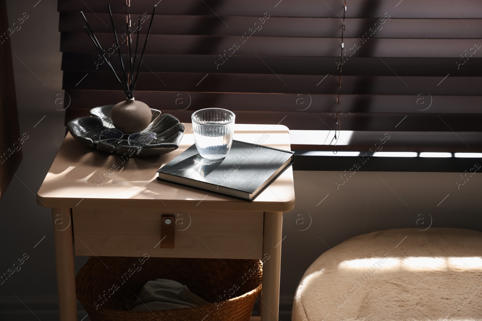 Wooden side table with glass of water, notebook and air reed diffuser indoors Photo of Wooden side table with glass of water, notebook and air reed diffuser indoors