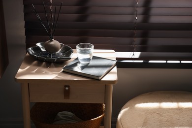 Photo of Wooden side table with glass of water, notebook and air reed diffuser indoors