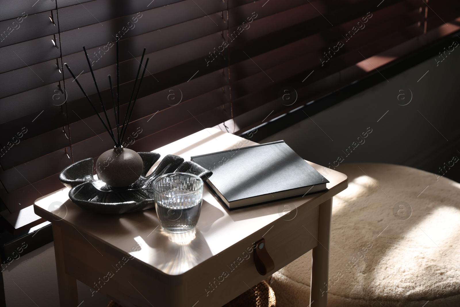 Wooden side table with glass of water, notebook and air reed diffuser indoors Photo of Wooden side table with glass of water, notebook and air reed diffuser indoors