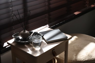 Photo of Wooden side table with glass of water, notebook and air reed diffuser indoors