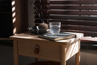 Photo of Wooden side table with glass of water, notebook and air reed diffuser indoors