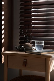 Photo of Wooden side table with glass of water, notebook and air reed diffuser indoors
