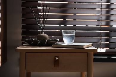 Photo of Wooden side table with glass of water, notebook and air reed diffuser indoors