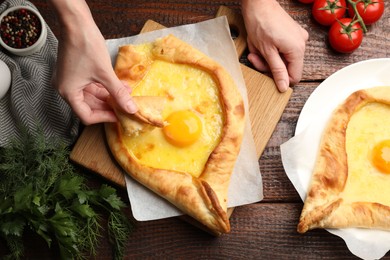 Photo of Woman eating delicious khachapuri at wooden table, top view