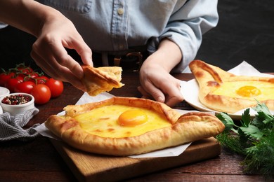 Photo of Woman eating delicious khachapuri at wooden table, closeup