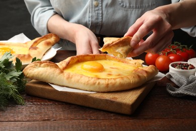 Photo of Woman eating delicious khachapuri at wooden table, closeup