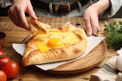 Photo of Woman eating delicious khachapuri at wooden table, closeup