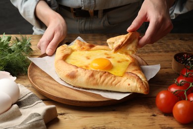 Photo of Woman eating delicious khachapuri at wooden table, closeup