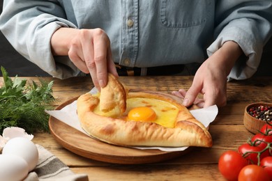 Photo of Woman eating delicious khachapuri at wooden table, closeup