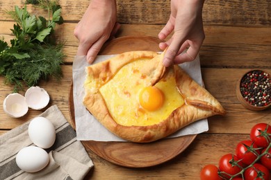 Photo of Woman eating delicious khachapuri at wooden table, top view