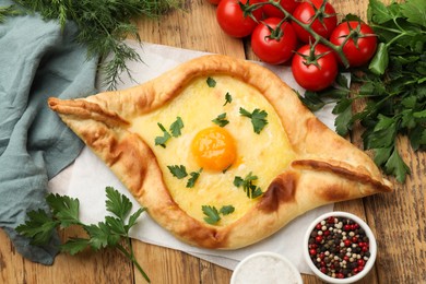 Photo of Tasty khachapuri with cheese, egg, tomatoes, parsley and spices on wooden table, flat lay
