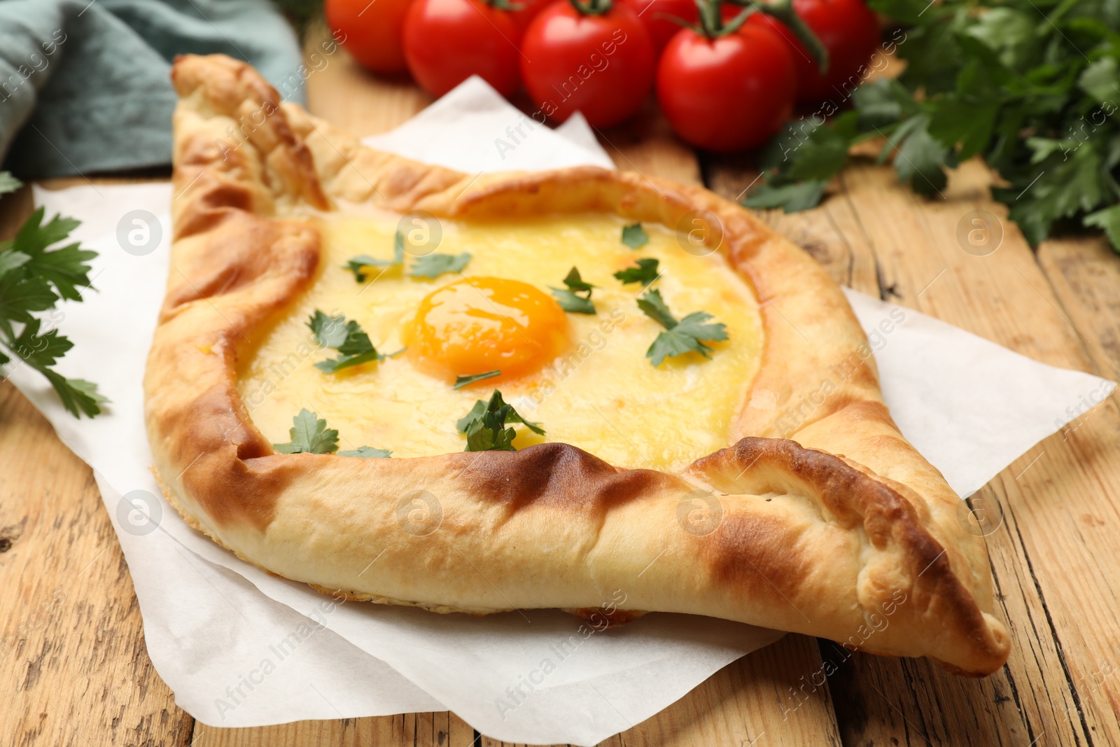 Tasty khachapuri with cheese, egg, tomatoes and parsley on wooden table, closeup Photo of Tasty khachapuri with cheese, egg, tomatoes and parsley on wooden table, closeup