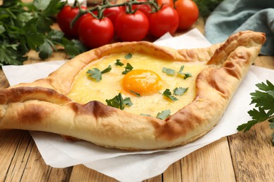 Photo of Tasty khachapuri with cheese, egg, tomatoes and parsley on wooden table, closeup