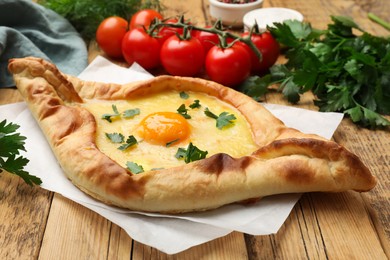 Photo of Tasty khachapuri with cheese, egg, tomatoes and parsley on wooden table, closeup