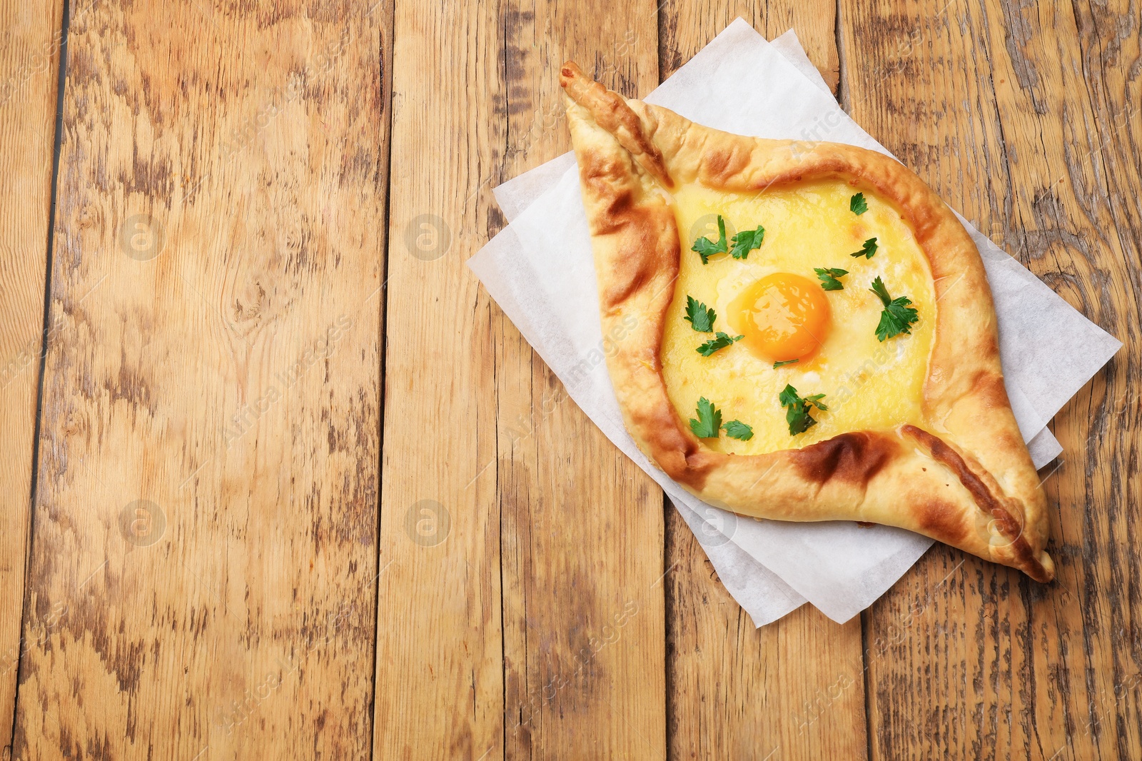Tasty khachapuri with cheese, egg and parsley on wooden table, top view. Space for text Photo of Tasty khachapuri with cheese, egg and parsley on wooden table, top view. Space for text