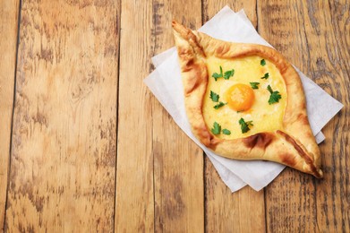 Photo of Tasty khachapuri with cheese, egg and parsley on wooden table, top view. Space for text