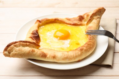 Photo of Tasty khachapuri with cheese, egg and fork on wooden table, closeup