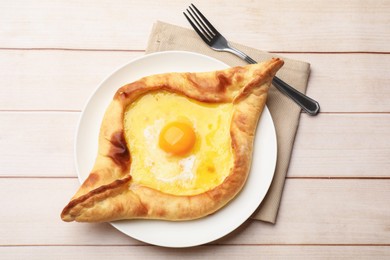Photo of Tasty khachapuri with cheese, egg and fork on wooden table, top view