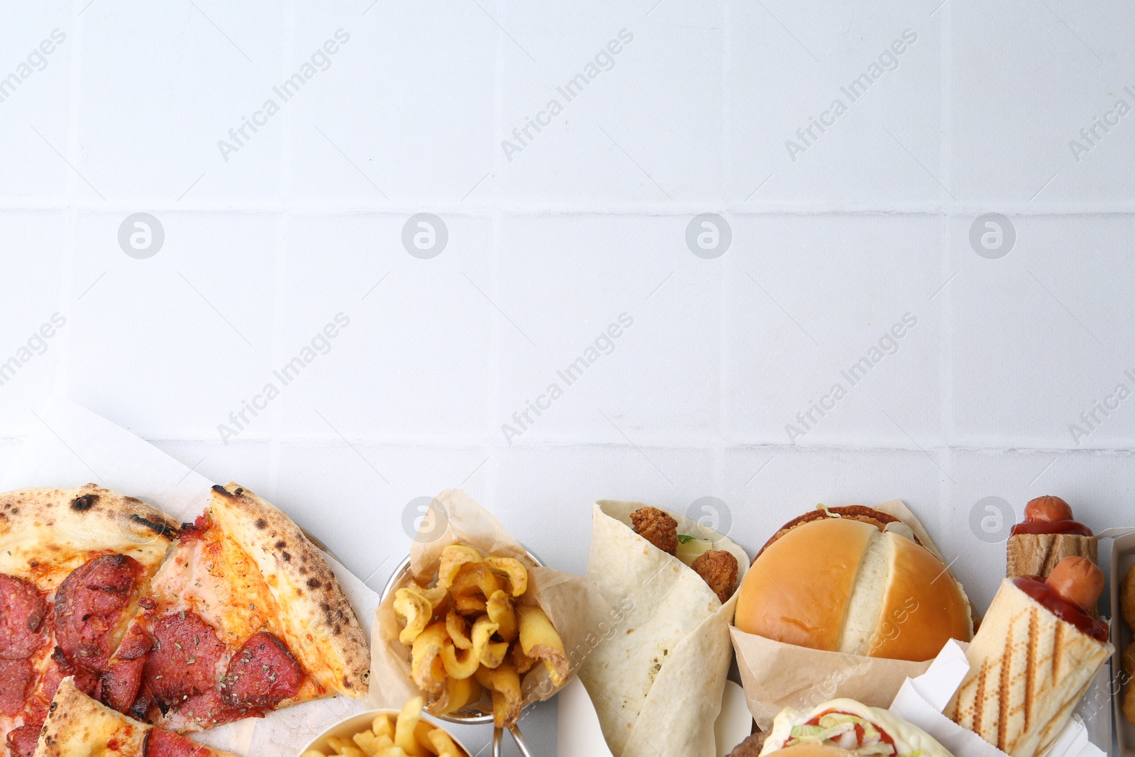 Different delicious fast food on white tiled table, flat lay. Space for text Photo of Different delicious fast food on white tiled table, flat lay. Space for text
