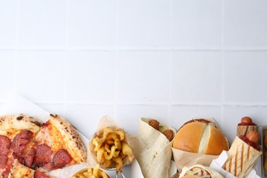 Photo of Different delicious fast food on white tiled table, flat lay. Space for text