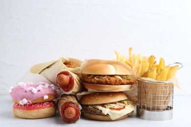 Photo of Different delicious fast food on white table, closeup