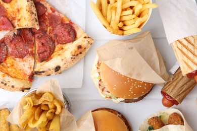 Photo of Different delicious fast food on white tiled table, flat lay