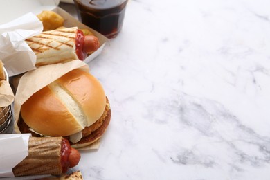 Photo of Different delicious fast food and soda drink on white marble table, closeup. Space for text