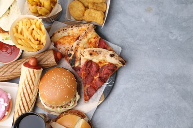Photo of Different delicious fast food and soda drink on grey table, flat lay. Space for text