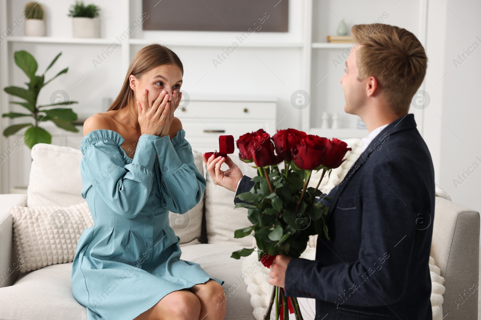 Man with engagement ring and bouquet of roses making marriage proposal to his excited girlfriend at home Photo of Man with engagement ring and bouquet of roses making marriage proposal to his excited girlfriend at home