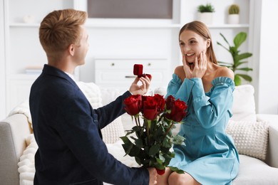 Photo of Man with engagement ring and bouquet of roses making marriage proposal to his happy girlfriend at home
