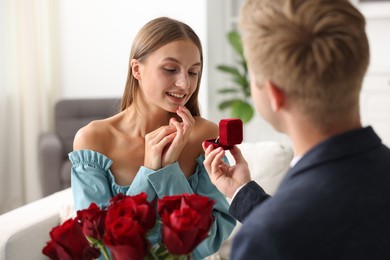 Photo of Man with engagement ring and bouquet of roses making marriage proposal to his happy girlfriend at home