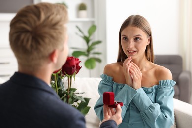 Photo of Man with engagement ring and bouquet of roses making marriage proposal to his happy girlfriend at home
