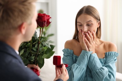 Photo of Man with engagement ring and bouquet of roses making marriage proposal to his happy girlfriend at home, closeup