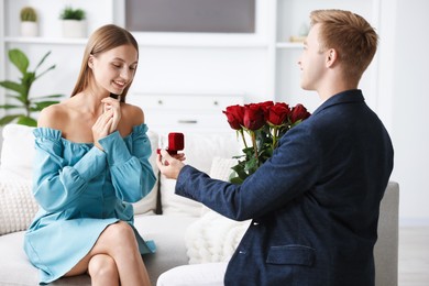 Photo of Man with engagement ring and bouquet of roses making marriage proposal to his happy girlfriend at home