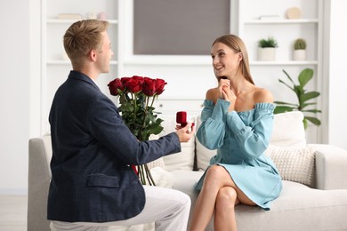 Photo of Man with engagement ring and bouquet of roses making marriage proposal to his happy girlfriend at home