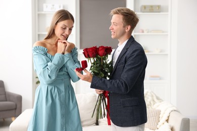 Photo of Man with engagement ring and bouquet of roses making marriage proposal to his happy girlfriend at home