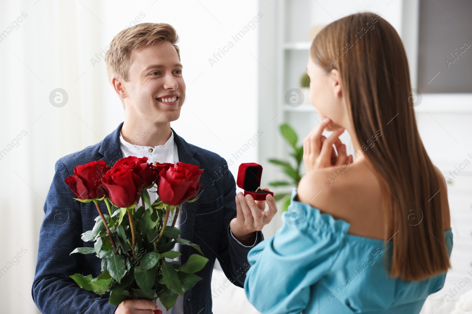 Smiling man with engagement ring and bouquet of roses making marriage proposal to his girlfriend at home Photo of Smiling man with engagement ring and bouquet of roses making marriage proposal to his girlfriend at home