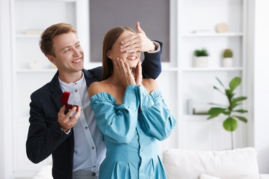 Photo of Making marriage proposal. Smiling man with engagement ring surprising his girlfriend at home. Space for text