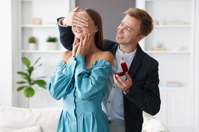 Photo of Making marriage proposal. Smiling man with engagement ring surprising his girlfriend at home