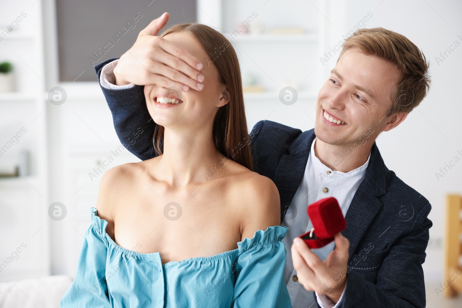 Making marriage proposal. Smiling man with engagement ring surprising his girlfriend at home Photo of Making marriage proposal. Smiling man with engagement ring surprising his girlfriend at home