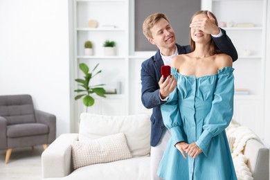 Photo of Making marriage proposal. Smiling man with engagement ring surprising his girlfriend at home. Space for text