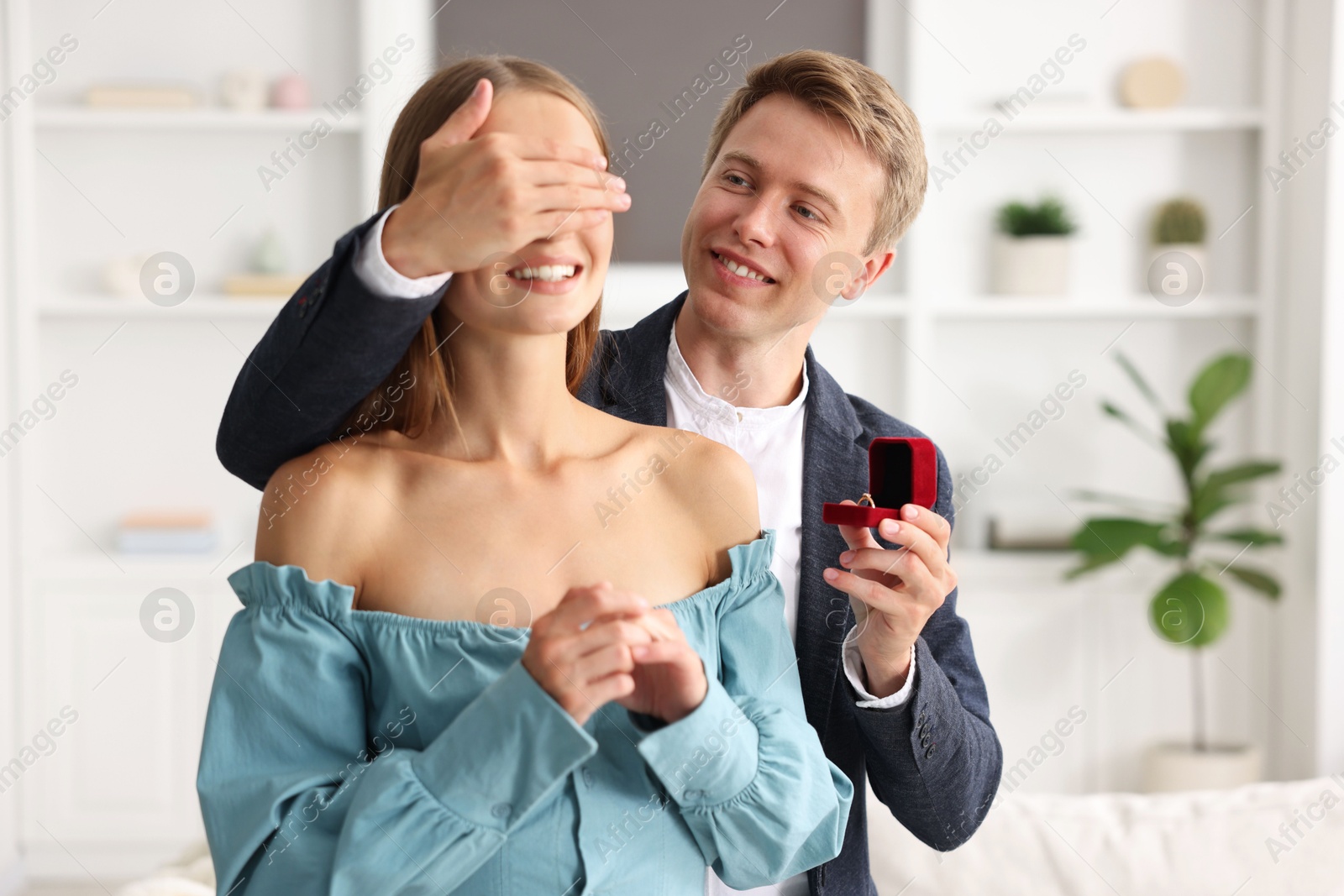 Making marriage proposal. Smiling man with engagement ring surprising his girlfriend at home Photo of Making marriage proposal. Smiling man with engagement ring surprising his girlfriend at home