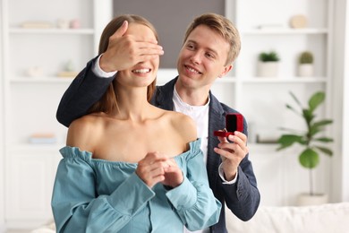 Photo of Making marriage proposal. Smiling man with engagement ring surprising his girlfriend at home
