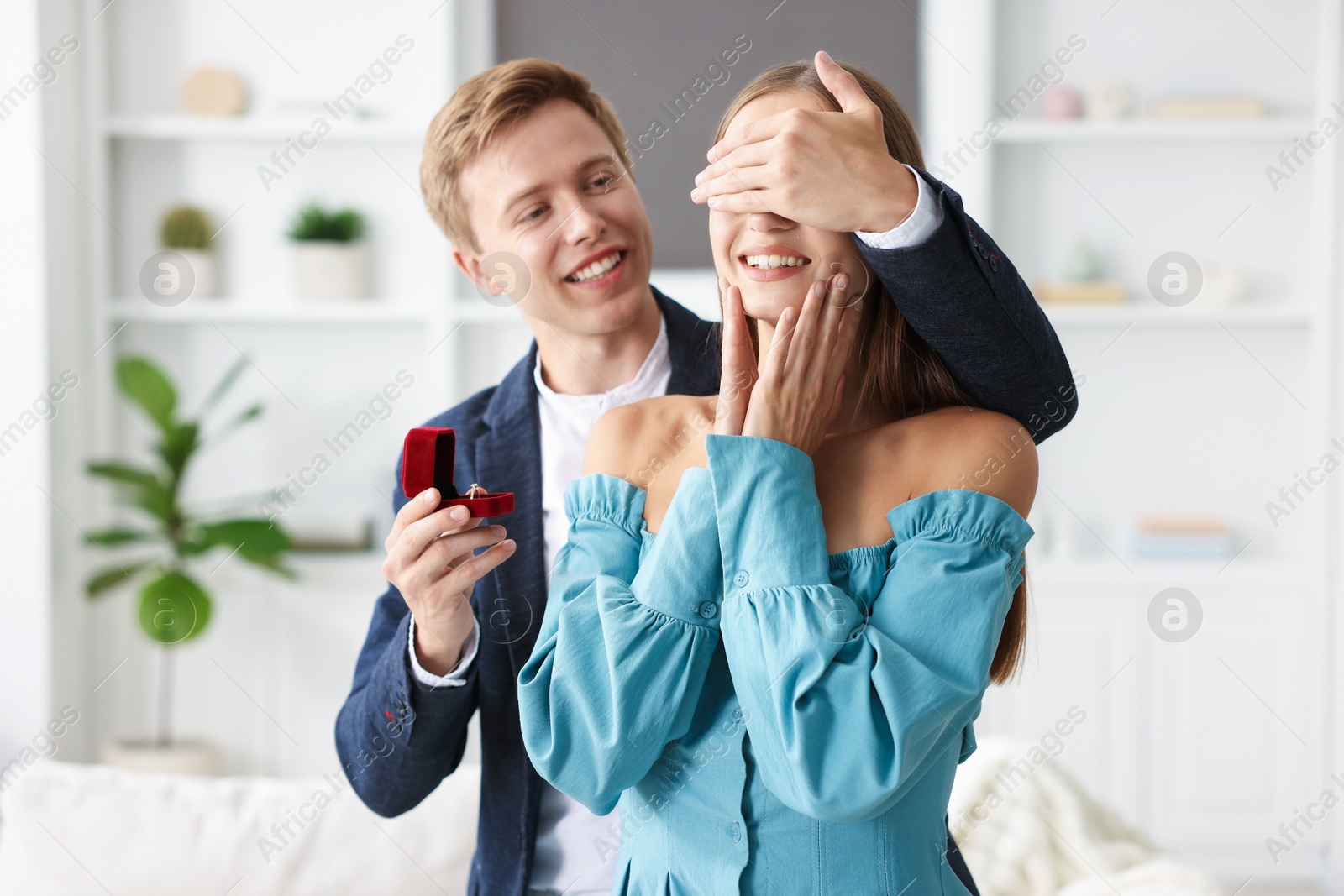 Making marriage proposal. Smiling man with engagement ring surprising his girlfriend at home Photo of Making marriage proposal. Smiling man with engagement ring surprising his girlfriend at home