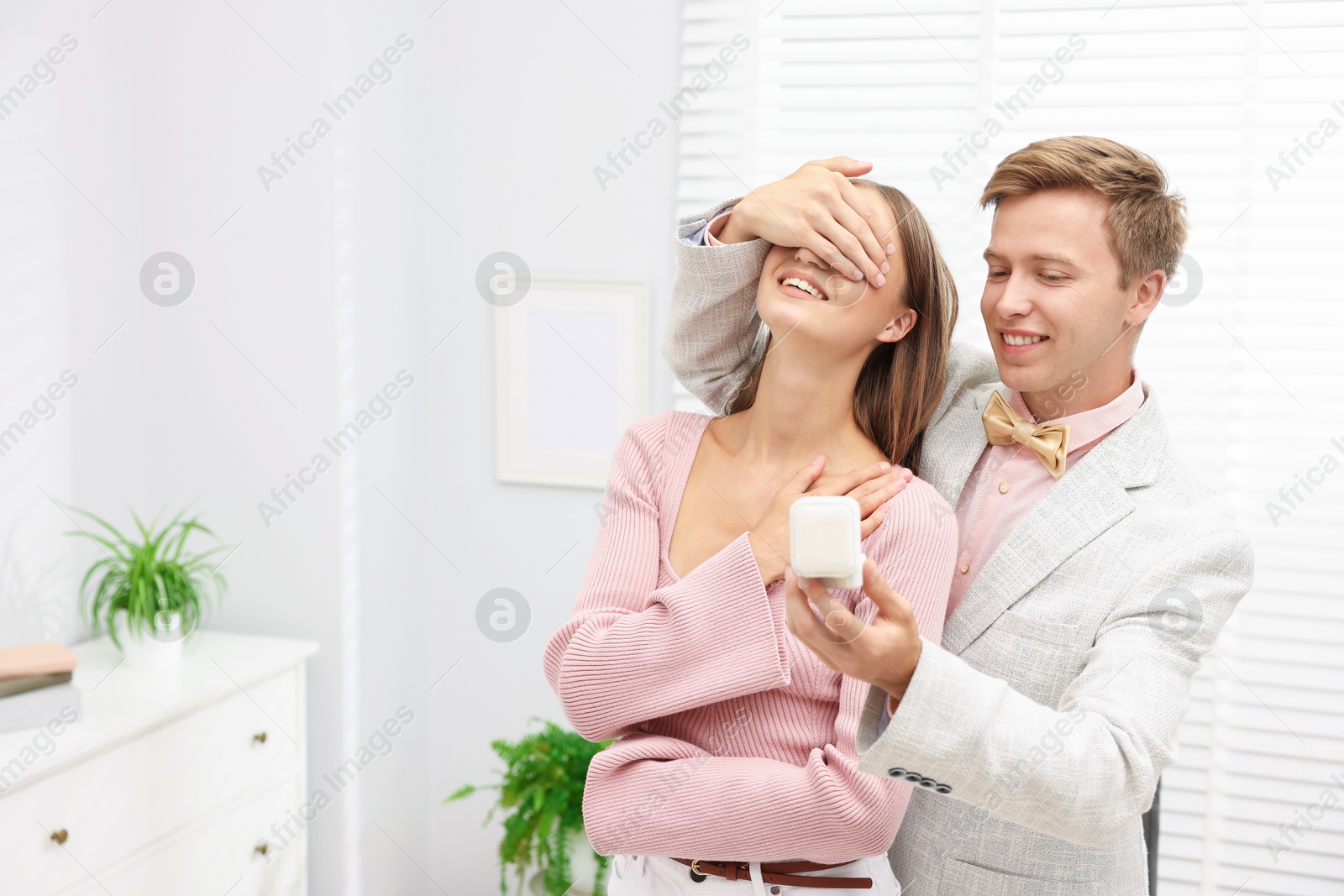 Making marriage proposal. Smiling man with engagement ring surprising his girlfriend in light room, space for text Photo of Making marriage proposal. Smiling man with engagement ring surprising his girlfriend in light room, space for text
