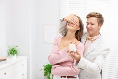 Photo of Making marriage proposal. Smiling man with engagement ring surprising his girlfriend in light room, space for text