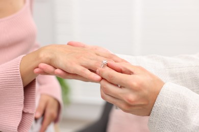 Photo of Making marriage proposal. Man putting engagement ring onto his girlfriend's finger at home, closeup