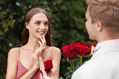Photo of Man with engagement ring and bouquet of roses making marriage proposal to his smiling girlfriend outdoors, closeup